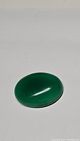 Oval vivid green onyx cabochon gemstone under normal light. Shows smooth polished surface and dark green color.