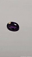 Oval cut deep purple Brazilian amethyst gemstone lying on a flat surface, showing facets and color variation.