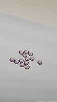 Photo of 18 small round cut purple amethyst gemstones on white background spread in a cluster.