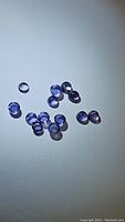 Group of multiple small round calibrated purple Iolite gemstones laid on a flat surface.