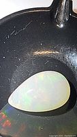 Close-up view of the pear-shaped cabochon Ethiopian opal showing milky white translucent body with play of color.