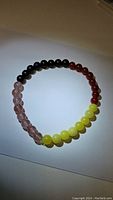 Full view of the gemstone stretchy bracelet arranged in a circle showing all four types of beads: light pink Strawberry Quartz, yellow Lemon Jade, black Onyx, and red Carnelian.