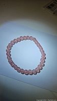Close-up frontal photo of the natural strawberry quartz bead bracelet placed flat on a white surface showing pink translucent beads and elastic string.