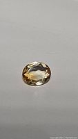 Close-up photo of an oval cut natural golden citrine gemstone, faceted and polished, showing clarity and color.