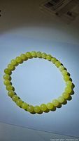 Photo showing natural lemon jade bracelet composed of smooth round yellow beads on stretchy band, laid flat on a white surface.