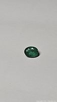 Close-up photo of the natural oval cut emerald gemstone showing its rich green color and clarity on a neutral background.