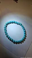 Photo of stretchy turquoise bead bracelet laid flat on white surface with soft lighting highlighting bead color and surface.
