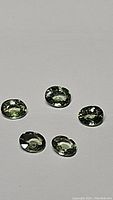 Five oval mint green sapphires laid on a flat white surface, each displaying clarity and transparent quality.