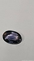 Oval cut purple blue sapphire gemstone on a plain neutral background, showing top view with faceted surface and color play.