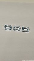 Three emerald cut sky blue topaz gemstones laid out in a row on a flat surface with a neutral background.