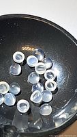 Multiple calibrated round white moonstone cabochons, approximately 3mm diameter each, showing translucence and catseye effect in dome shape.