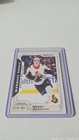 Photo of a Brady Tkachuk rookie hockey card in a protective plastic sleeve, showing the player in Ottawa Senators uniform with 'Marquee Rookie' text.