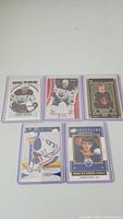 Five hockey cards featuring Connor McDavid in protective sleeves with various designs and team colors.