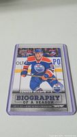 Front view of a Connor McDavid Upper Deck rookie hockey card. The card highlights the Biography of a Season insert with season highlights and stats, showing McDavid in his Edmonton Oilers blue and orange jersey.