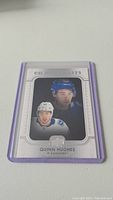 Photo of a Quinn Hughes rookie hockey card from Upper Deck, featuring dual images of Hughes in Vancouver Canucks gear, with silver frame and Rookie Stars label.