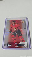 Photo shows Tim Stutzle rookie hockey card with player in red Ottawa Senators uniform. Card is glittery with holographic elements and is encased in protective plastic.
