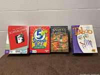 Four boxed board games displayed side by side on a surface against a wall: Scattergories, 5 Second Rule, Snakes and Ladders, and Taboo.