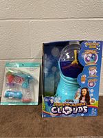 Gazillion Burstin Bubble Clouds bubble machine and light up bubble blower together in original packaging against a wall background.