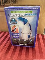 Front view of the original packaging box showing product name, power specifications (1100 watts), steam nozzle image, and key features like high velocity continuous steam.