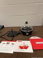 Full view of Dash Rapid Egg Cooker with clear plastic lid and black egg tray, along with manuals.