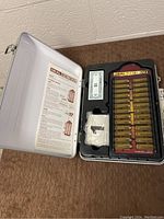 Opened silver briefcase with game board, cards, play money, and instructions inside lid.