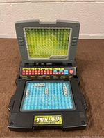 Closed-up view of open Electronic Battleship Advanced Mission game showing green LED display, control panel with colored buttons, and blue grids with ships.