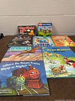 Photo showing 12 children's books including Garfield comic book, Phonics Patrol Step into Reading boxed set, dinosaur book, Brer Rabbit storybook, steam trains book, and others.