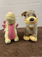 Both plush toys side by side on brown surface against a light brick wall, showing size and color contrast.