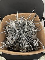 Box filled with assorted metal hooks for slat walls and pegboards, showing hooks scattered inside a cardboard box.