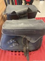 View of one saddle bag showing top flap and buckle straps on red surface