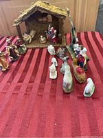 Overall view of the nativity set showing stable, figurines in front on a red striped fabric.