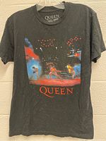Front view of black Queen band T-shirt with colorful concert photo graphic and red 'QUEEN' text under it.