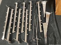 Eight long waterfall hooks with evenly spaced small knobs for hanging multiple items photographed on black surface.