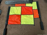 Two soccer referee flags with yellow and orange checkered patterns and black handles, one with protective cover.