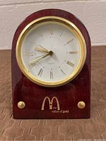 Front view of vintage McDonald's quartz clock with Roman numeral face, wooden base, and gold-tone trim