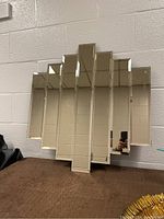 Front view of the 7-panel bevelled mirror showing stepped modernist design and reflections of a brick wall and ceiling.