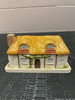 Front view of the cottage-shaped butter dish showing yellow thatched roof, brick chimney, white walls and ivy details.