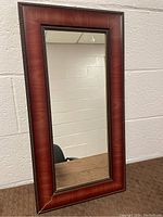Full view of the wall mirror showing the rectangular shape, brown textured frame with beaded inner edge, and clear reflective surface.