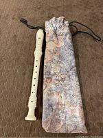Front view of Yamaha soprano recorder next to camouflage fabric drawstring case on brown textured surface