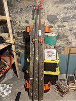 Two long 72 inch bar clamps standing vertically against a wall in a basement setting, showing overall length and used condition.