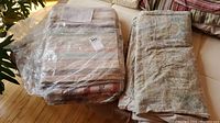 Folded paisley bedspread next to plastic-wrapped striped blanket on mattress