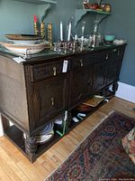 Side view of large dark wood buffet with carved floral designs on drawers and doors, turned legs and lower shelf with plates.