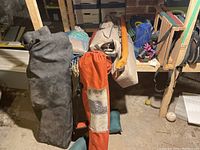 Photo of camping chairs in orange labeled 'Roots' carry bag and black/grey carry bag, along with additional beige and blue bags likely containing tent and cookware items on basement floor.