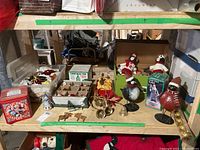 Wide view of shelf showing assortment of Christmas tree ornaments including boxed baubles, plush figures, bird figurines with Santa hats, small bells and miniature reindeer.