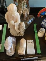 View of all three carved figurines on display on a black surface including a large robed figure, a lizard/salamander, and an abstract animal sculpture.