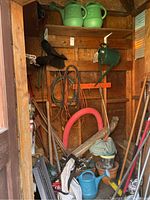 Shelved collection of garden watering cans, hose sprayers, gardening tools and pots in shed interior