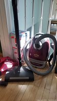 Full view of the Miele canister vacuum with hose, wand, and vacuum bags in the background