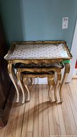 Three stacked vintage nesting tables with gold finish and patterned tile tops visible from front angle