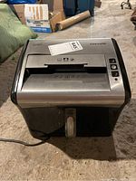Front view of the Staples Mailmate paper shredder showing the paper slot, buttons, and power cord on the left side.