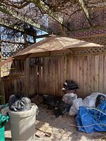 Full view of the cantilever umbrella with beige canopy, set up in an outdoor patio area with fencing and some storage items in the background.
